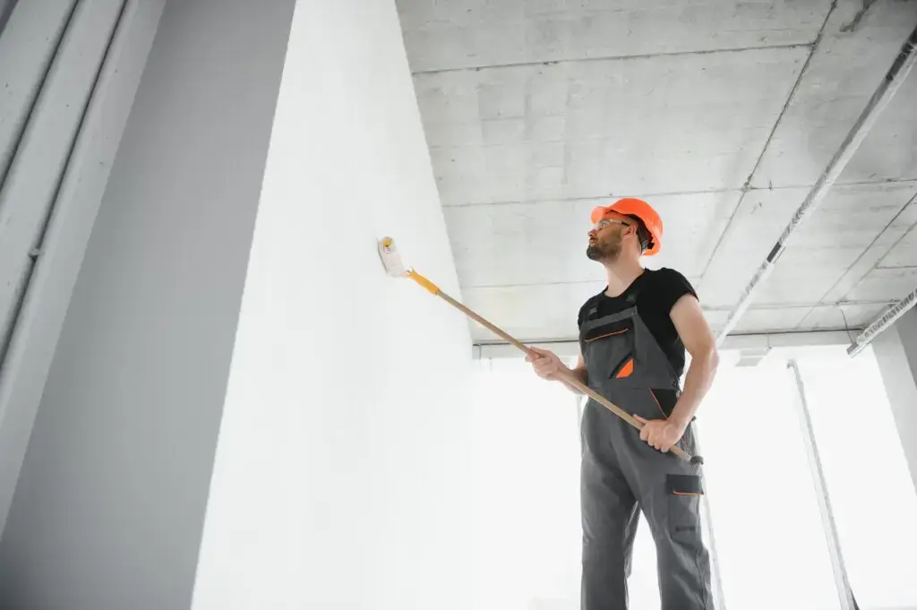 Portrait of man holding paint roller while painting white wall and making renovation.